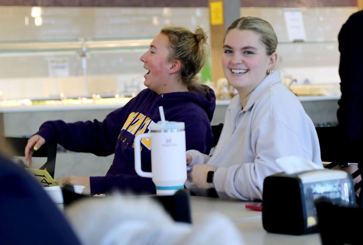 Two female students smile and laugh at a table in the Dining Hall