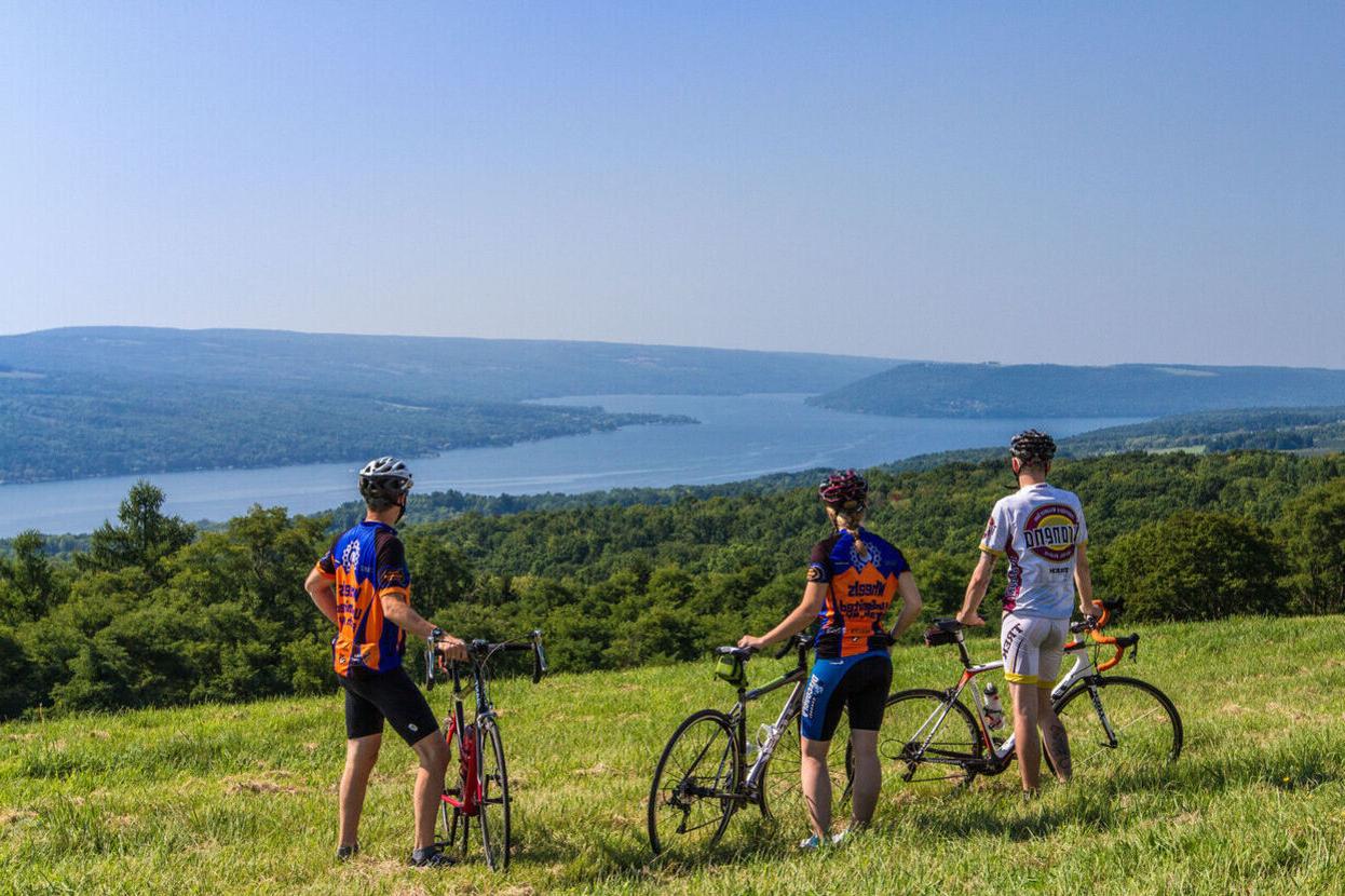 Three cyclists take a break in a a grassy area and look over Keuka Lake